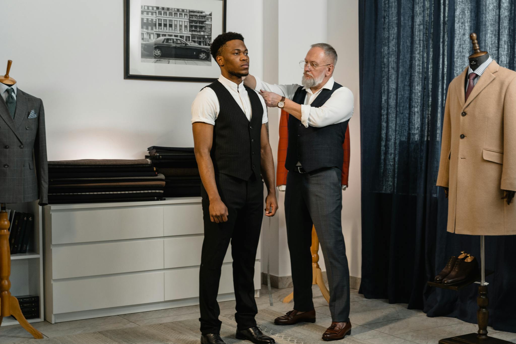 A tailor performs measurements on a man for a custom suit fitting in a professional studio.